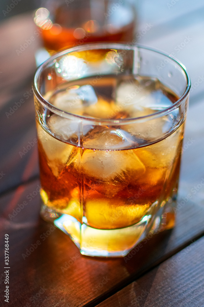 Two glasses of whiskey with ice cubes served on wooden planks. Two glasses of whiskey with ice cubes served on wooden planks.