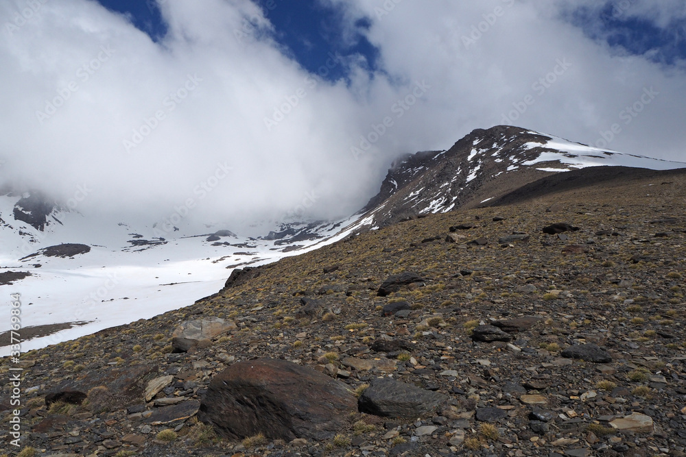The mountain landscape with the dark rocks covered by white snow, the far peak, the cloudy sky.