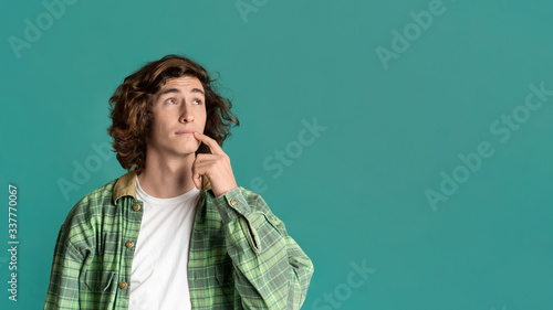 Thoughtful young guy pondering over idea on turquoise background, blank space. Panorama