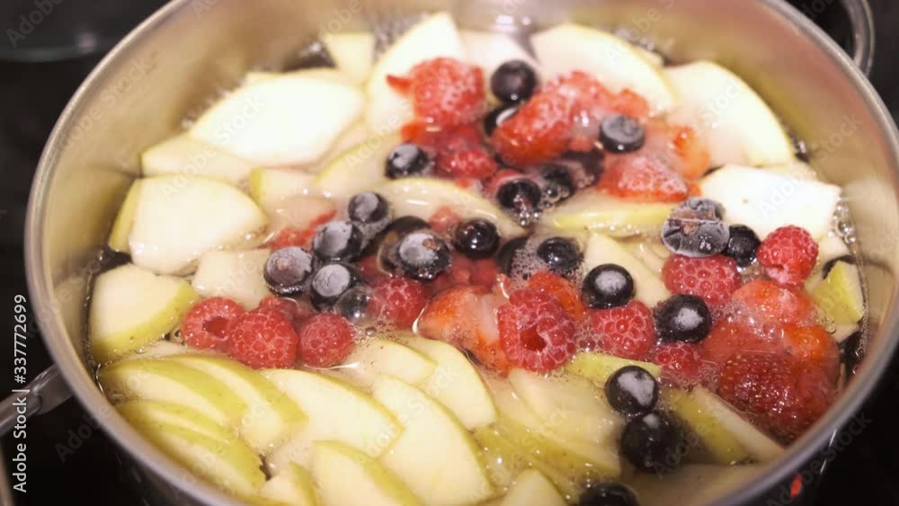 Cooking sweet delicious healthy homemade compote drink from tasty apples and frozen berries in a steel sauce pan Cooking sweet delicious healthy homemade compote drink from tasty apples and frozen berries in a steel sauce pan