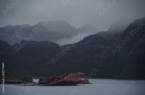 Shipwreck SS Santa Leonor or wreck of sunk ship in Chilean Fjords in Magellan Strait or Beagle Channel in Patagonia bay with mountains in fog or foggy, misty and mystical atmosphere landscape scenery photo