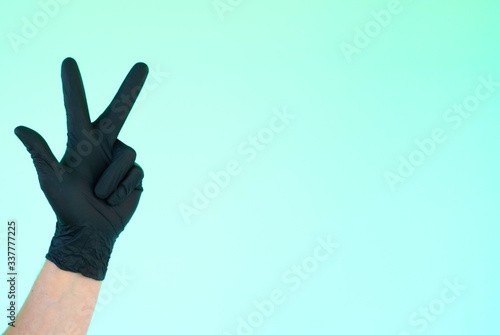 hand in sterile black gloves on a turquoise background shows different signs and symbols with fingers