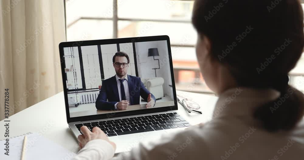 Confident businessman online coach, mentor wearing suit video calling by webcam in conference chat professional training talking to client interviewing candidate on laptop screen. Over shoulder view. Confident businessman online coach, mentor wearing suit video calling by webcam in conference chat professional training talking to client interviewing candidate on laptop screen. Over shoulder view.