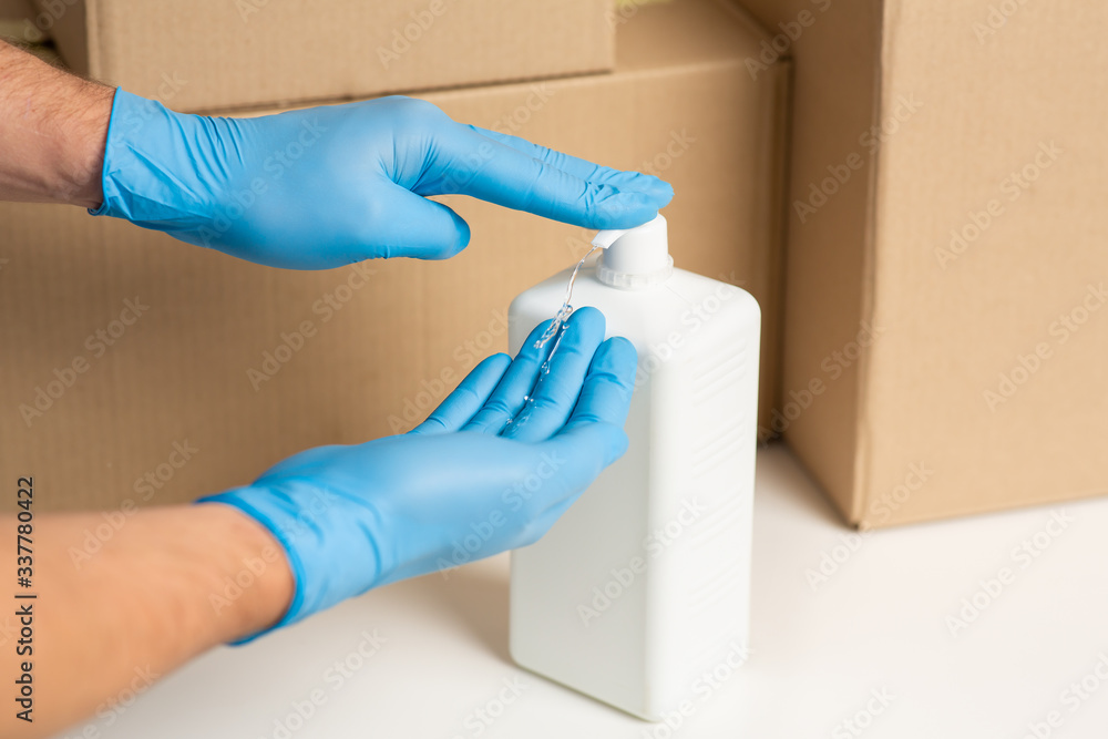Obraz premium Deliveryman disinfects hands. Cardboard boxes at background
