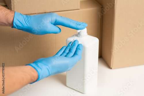 Deliveryman disinfects hands. Cardboard boxes at background