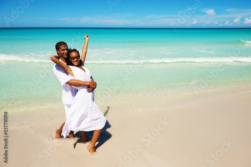 Happy, young couple hugging at the tropical beach, looking at camera. Copy space