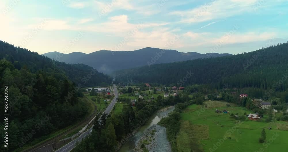 Aerial view of the beautiful mountains and the village on the hill. Drone shot of a village in the mountains at sunset, summer evening mountain landscape with river and road backround 4k Aerial view of the beautiful mountains and the village on the hill. Drone shot of a village in the mountains at sunset, summer evening mountain landscape with river and road backround 4k