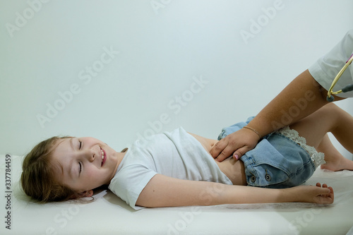 doctor pediatrician checks the stomach of a child lying on a couch. The surgeon palpates the girl’s stomach in his hospital room