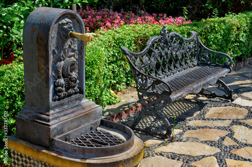 Old iron public street tap for fresh water  near the iron bench. Typical andalusian style, Estepona, Spain.