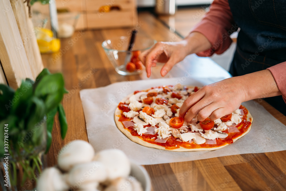 Woman's hands adding cherry tomatoes to a traditional margarita pizza. Preparation of a Original Italian pizza