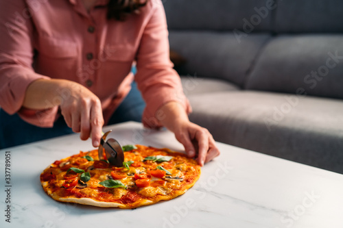 Woman cutting a traditional italian margarita pizza in her living room. Stay at home