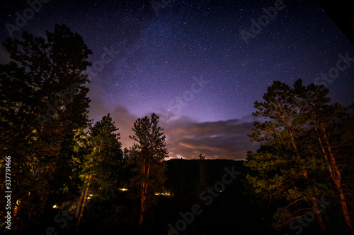 A starry sky over the mountainous region of Bailey, Colorado with the lights of Denver, Colorado in the background.