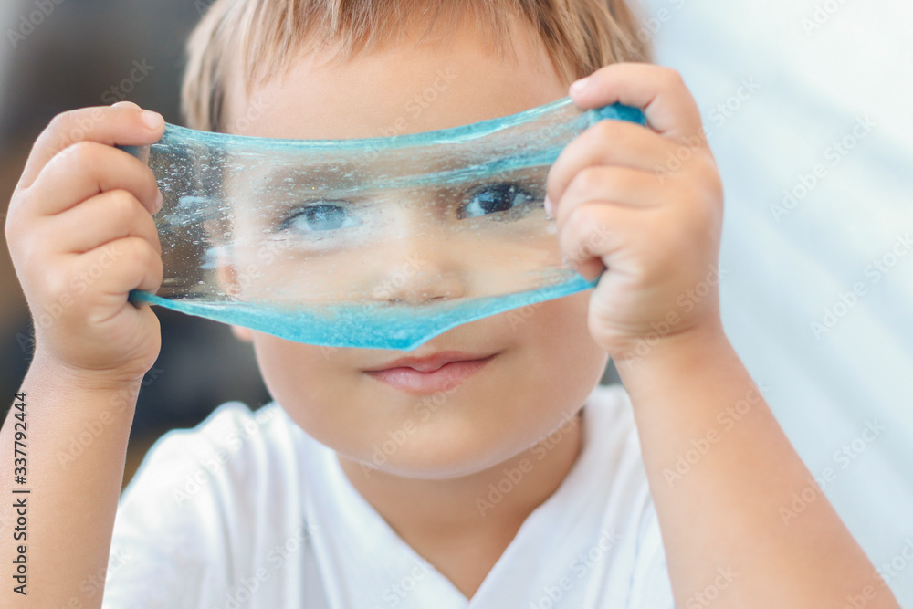 The kid plays with a toy called slime, stretches and sculpts fun on his face. The child is having fun with a creative scientific experiment The kid plays with a toy called slime, stretches and sculpts fun on his face. The child is having fun with a creative scientific experiment