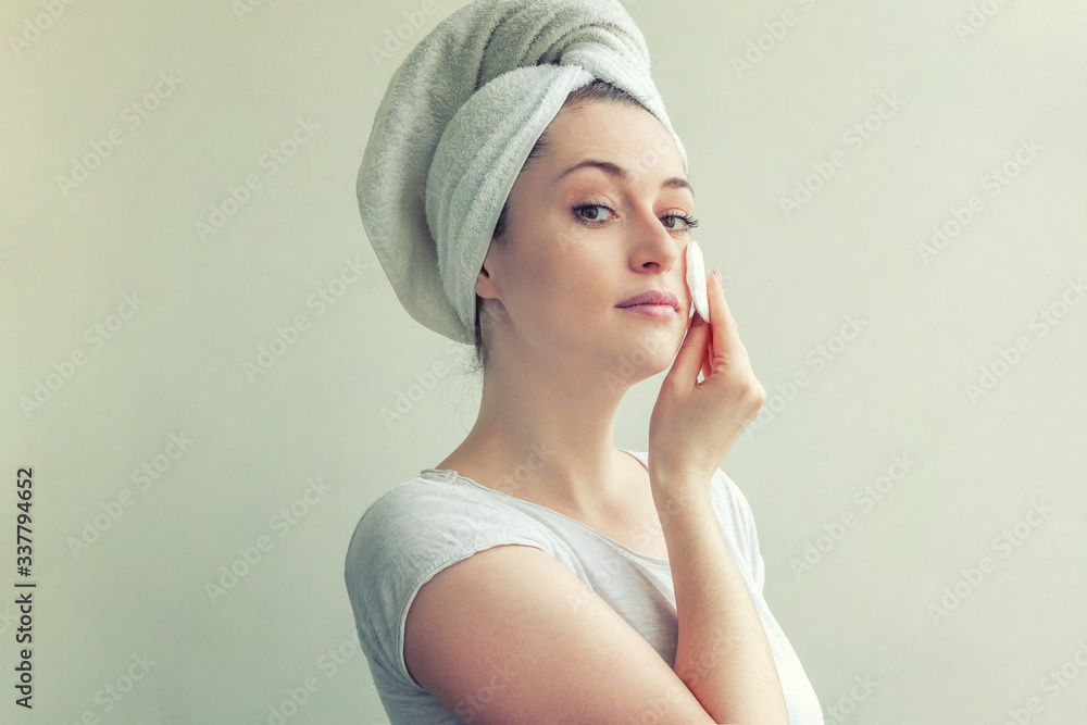 Smiling woman in towel on head with soft healthy skin removing make up with cotton pad isolated on white background Smiling woman in towel on head with soft healthy skin removing make up with cotton pad isolated on white background