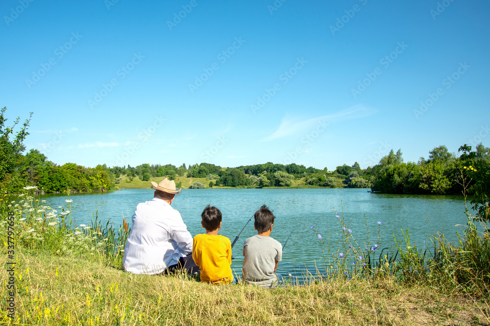 Two boys and grandfather are fishing on  a pond.  They are surrounded by beautiful nature.  Fishing is a dream for children.