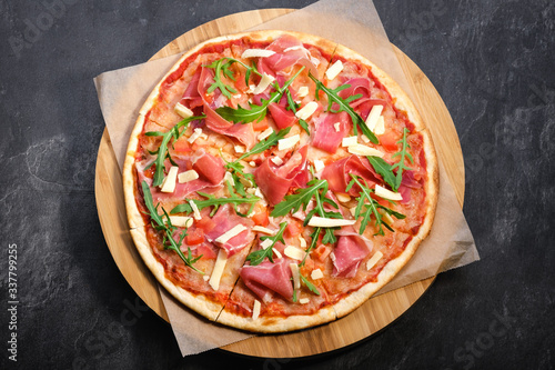 Pizza on wooden board on black stone background. Italian traditional food. Delicious pizza with serrano jamon, parmigiano-reggiano cheese and rucola. Restaurant menu. Copy space, top view
