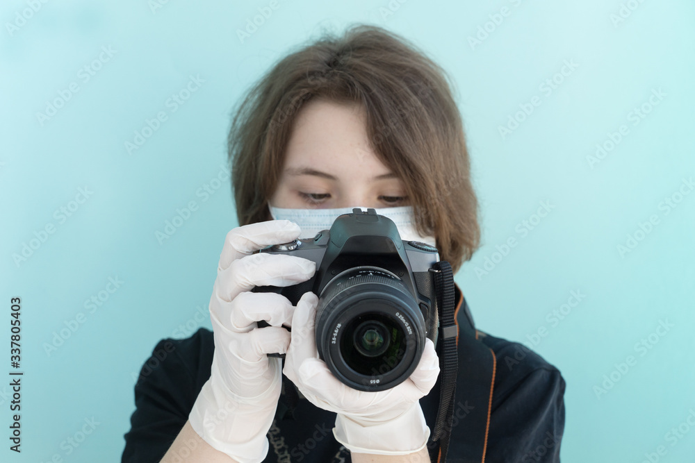 young female photographer in medical mask and white medical gloves makes photos with her camera on light blue backgrouund, protection from viruses and coronavirus pandemic, health care concept young female photographer in medical mask and white medical gloves makes photos with her camera on light blue backgrouund, protection from viruses and coronavirus pandemic, health care concept