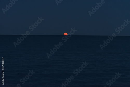 Orange moon rising on ocean horizon 