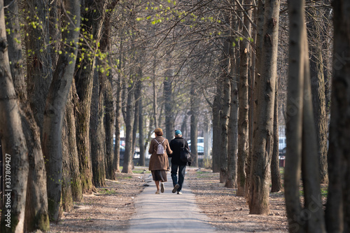 man and woman spend time outdoors. cute couple in caps walk along the alley between the trees on a spring day