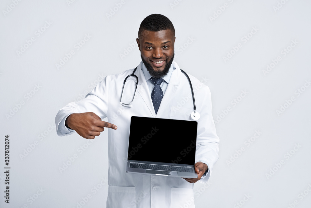 Black cheerful doc pointing at blank laptop screen Black cheerful doc pointing at blank laptop screen
