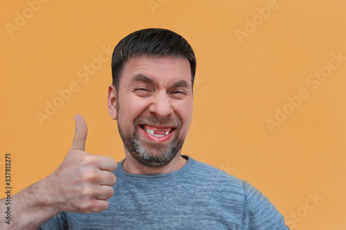 Photo cheerful charismatic bearded young man with no front upper teeth gives a thumbs