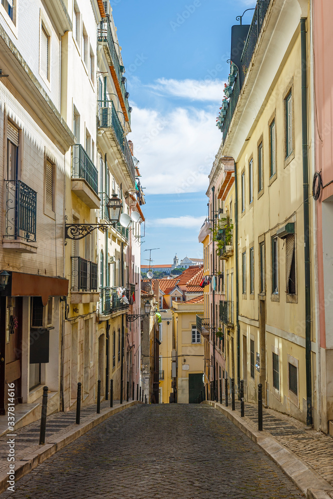 Old residential buildings along an empty, narrow and idyllic cobblestoned street in the Baixa district in Lisbon, Portugal, on a sunny day.