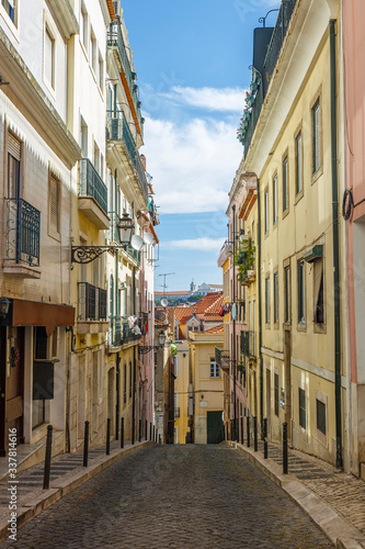 Old residential buildings along an empty, narrow and idyllic cobblestoned street in the Baixa district in Lisbon, Portugal, on a sunny day.