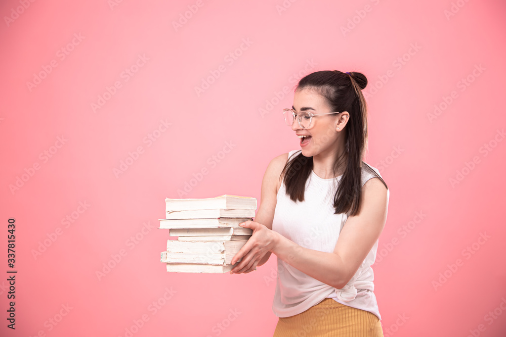 Portrait of a young woman with glasses on a pink background with books in her hands . Portrait of a young woman with glasses on a pink background with books in her hands .