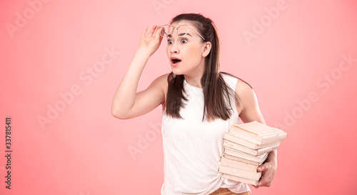 Portrait of a young woman with glasses on a pink background with books in her hands .