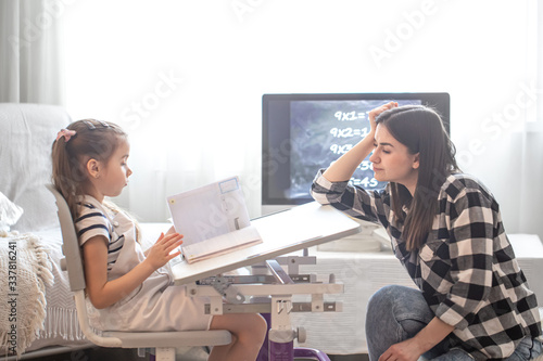 A mother with a child sits at the table and does homework. The child learns at home. Home schooling.