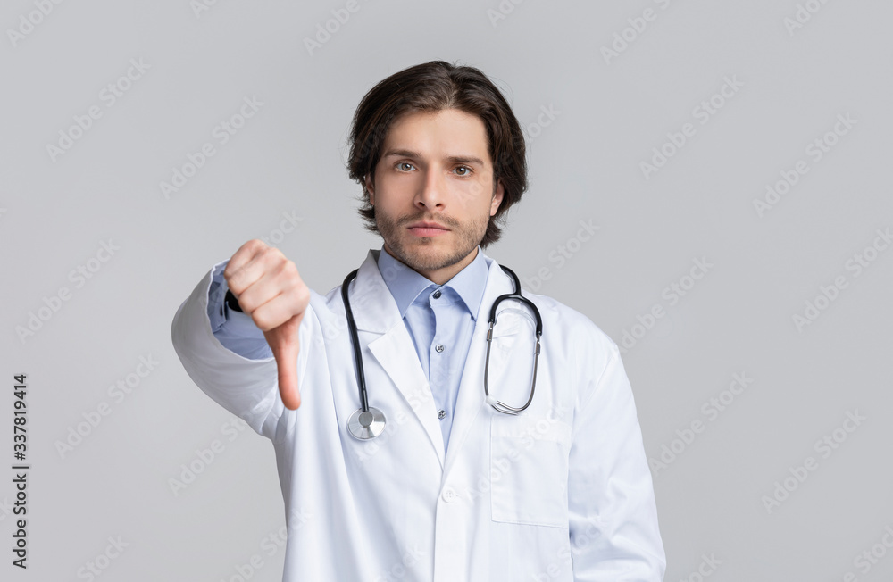 Portrait of serious confident young doctor showing thumb down gesture Portrait of serious confident young doctor showing thumb down gesture
