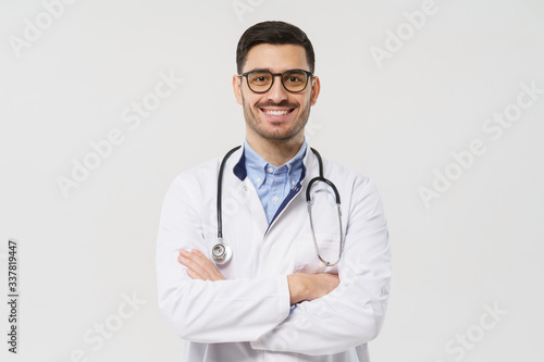 Portrait of smiling handsome male doctor with stethoscope around neck, wearing white coat and round glasses, isolated on gray background