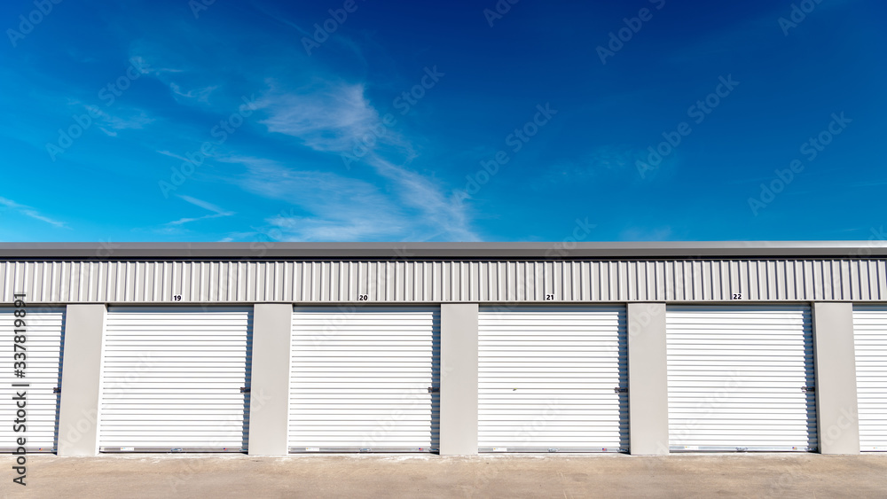 Mini storage garages lines up next to one another with blue sky and clouds