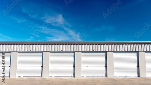 Slika na platnu Mini storage garages lines up next to one another with blue sky and clouds