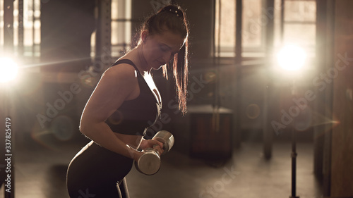 Candid strong young woman is training with a dumbbells in the gym. Real wokout photo