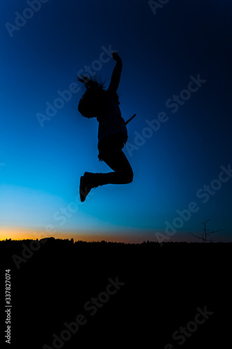 Silhouette of a girl in a jump on a background of sunset and a dark blue sky