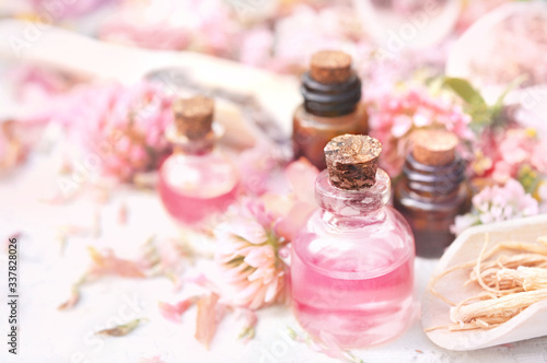 Essential oil bottles on pink clover flowers and medicinal herbs background, shallow DOF, toned