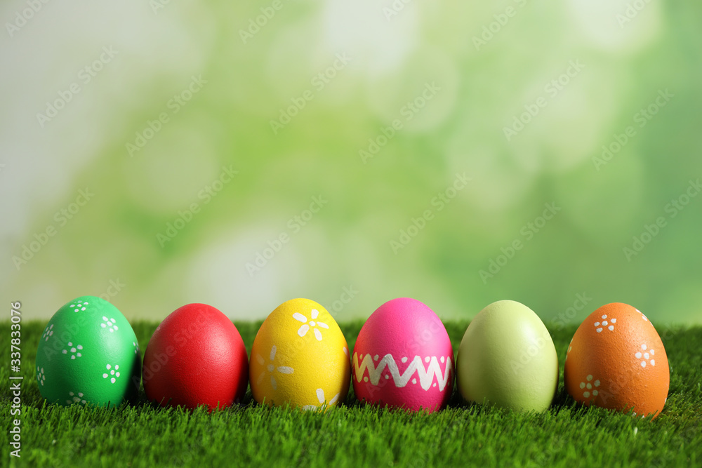 Colorful Easter eggs on green grass against blurred background. Space for text