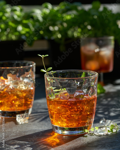 orange summer cocktail with ice on dark background. Shadows of glasses, hard sun light.