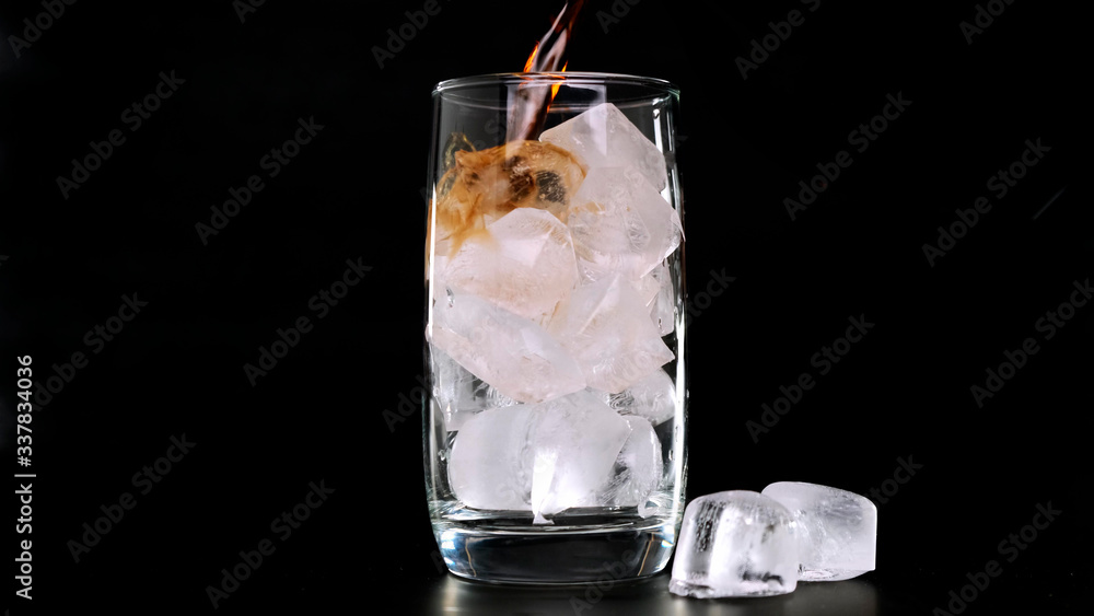 Pouring Cola with ice cubes in glass on black background. Close up. Pouring Cola with ice cubes in glass on black background. Close up.