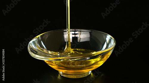 Honey pouring in glass bowl on black background. Close up.