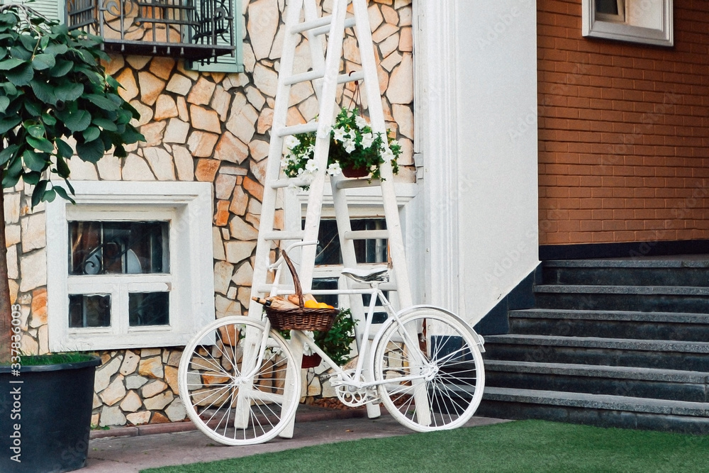 White bicycle with a basket in front of house