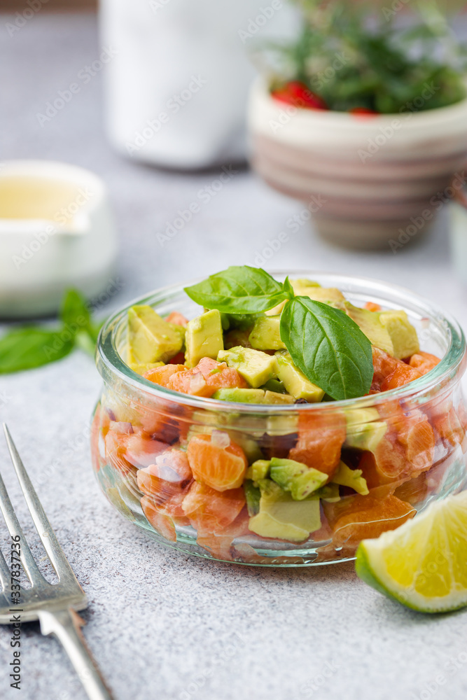 Delicious avocado and raw salmon salad, tartare, served glass jar with lime, light background Delicious avocado and raw salmon salad, tartare, served glass jar with lime, light background
