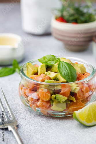 Delicious avocado and raw salmon salad, tartare, served glass jar with lime, light background