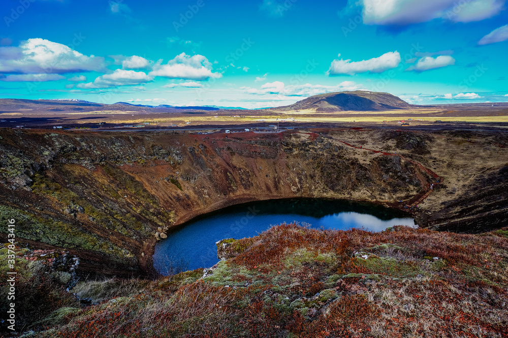 The Kerid Volcanic crater and the deep water lake at the bottom of the volcano surrounded by the volcanic red rocks and moss and lichen