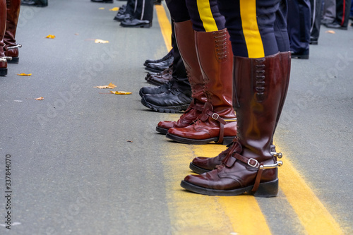 Police officers standing on a yellow line in the middle of a paved road. The officers have a yellow stripe on their pants and brown leather boots. There are multiple rows of men on parade. photo