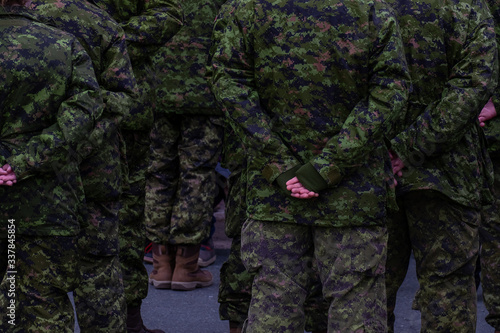 Military men standing in formation on parade wearing green camouflage uniforms while attending boot camp. The officers have their hands behind their backs standing at ease. 