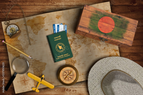 Top view of traveling gadgets, vintage map, magnify glass, hat and airplane model on the wood table background. On center, official passport of Bangladesh and your flag.