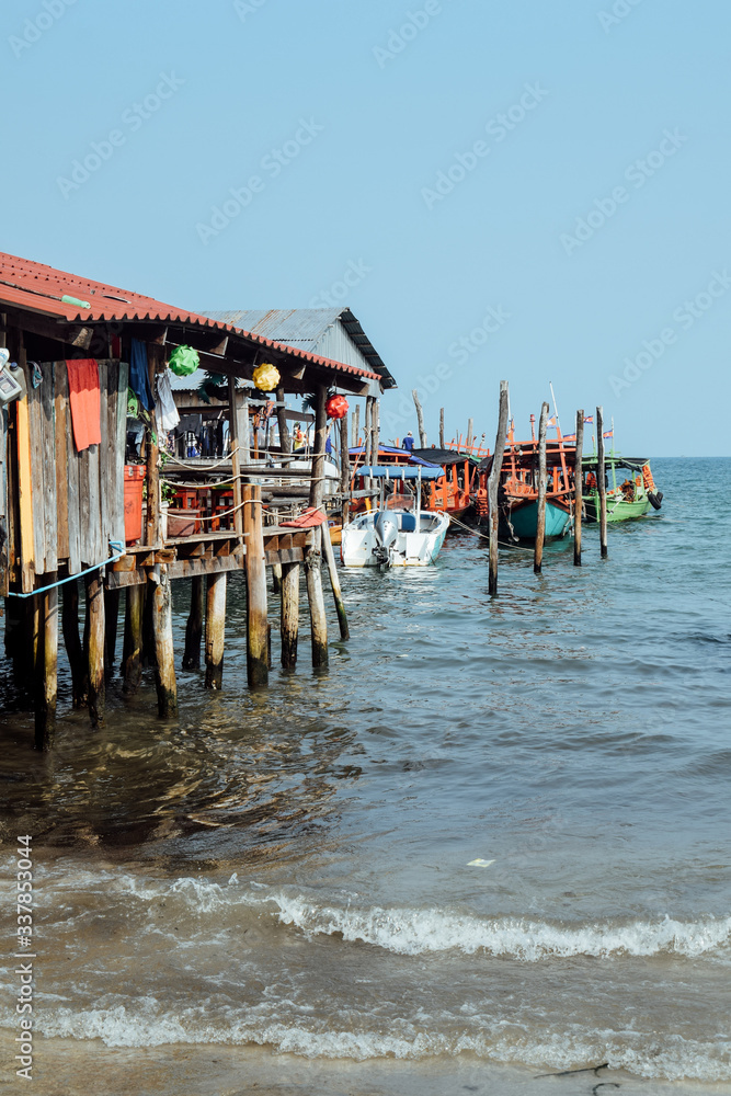 Sea waves around fisherman wooden boats docked by a pier on pylons