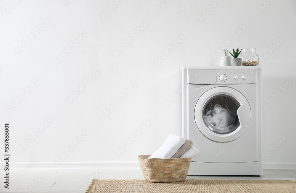 Modern washing machine and laundry basket near white wall indoors, space for text. Bathroom interior Modern washing machine and laundry basket near white wall indoors, space for text. Bathroom interior